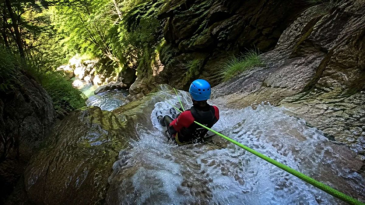 Barranquista con casco y neopreno descendiendo un tobogán de agua controlado